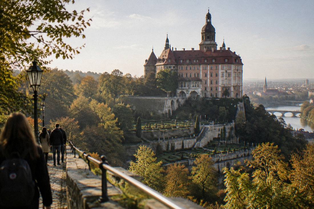 A large castle on a hill above a forested valley, with terraced gardens visible below the building.