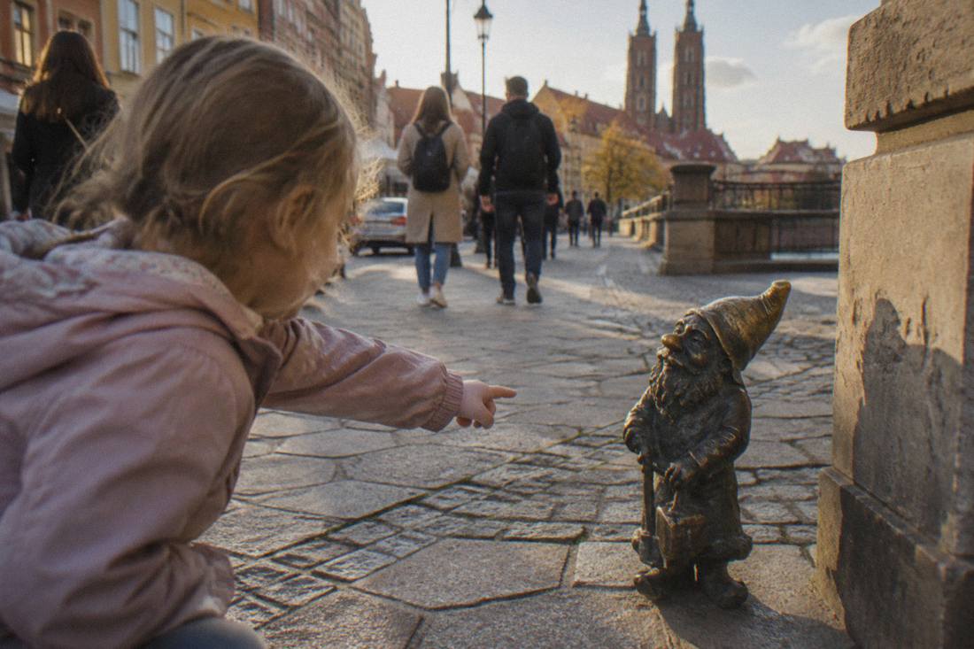 A child pointing at a small bronze dwarf statue on a Wroclaw sidewalk