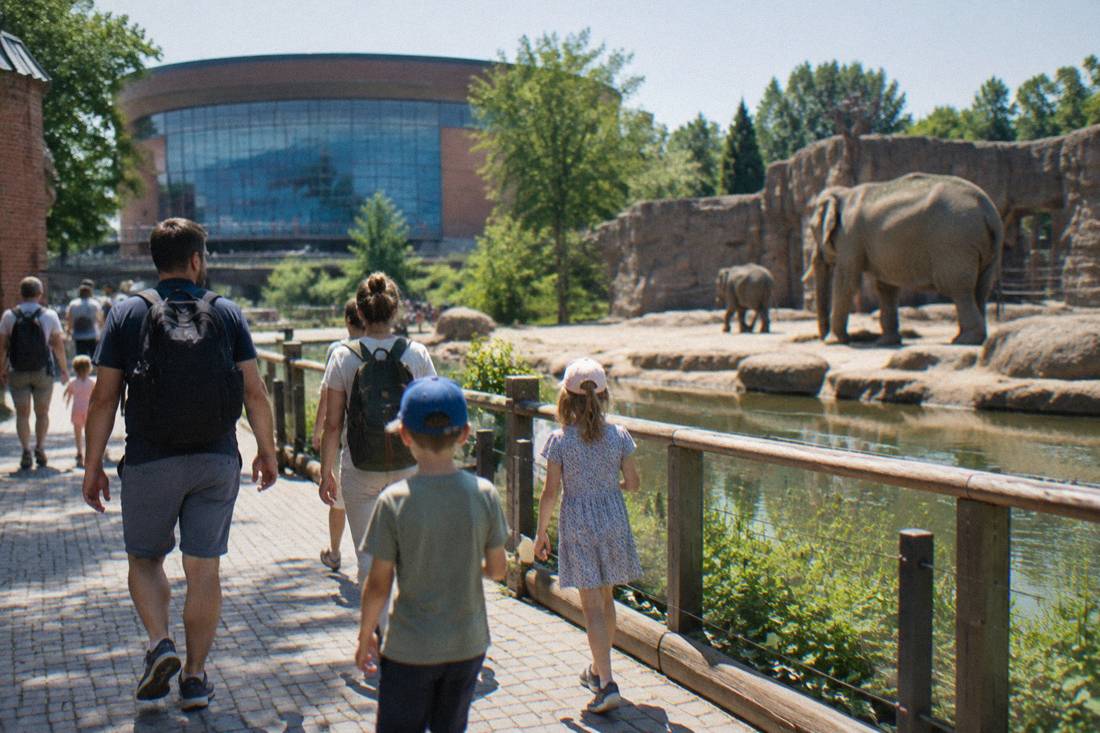 A family with children walking through Wroclaw Zoo past a large animal enclosure