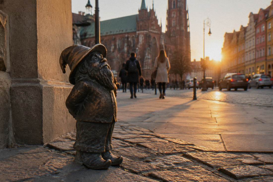 A bronze dwarf statue wearing a hat standing on a Wroclaw street corner